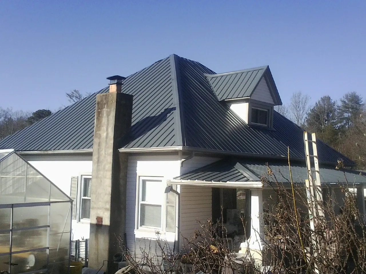 Dark blue standing seam metal roof on a white farmhouse with dormer — Slate & Tile Roof Repair by Roofing Brothers in Winger
