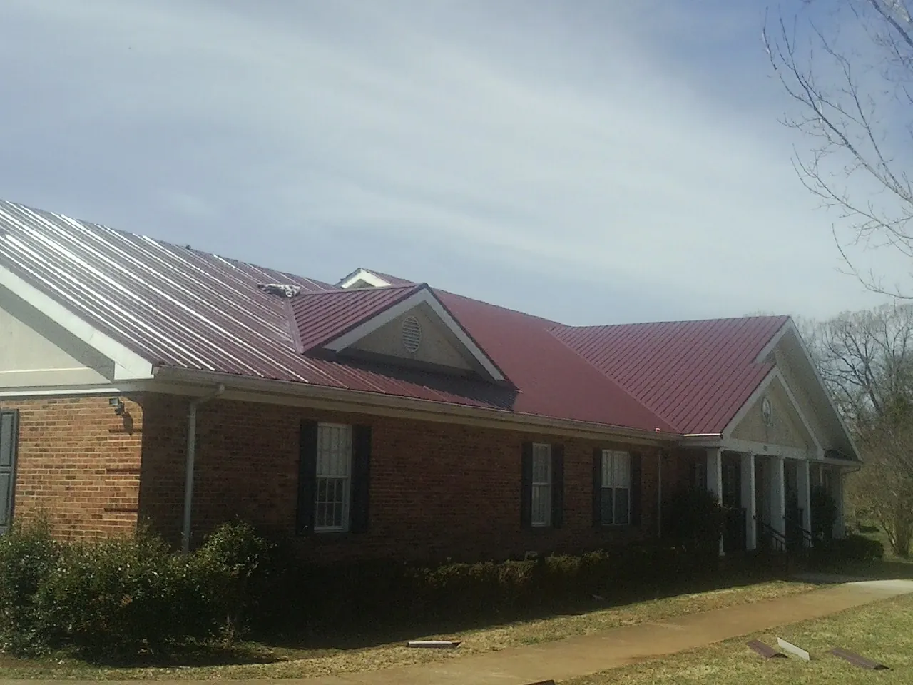 Red metal roof with gabled entries on a long brick building, from a Hail Damage Roof Repair job in Winger