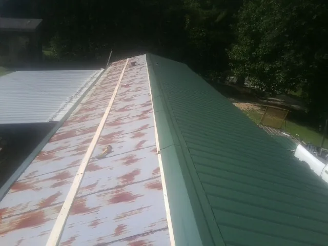 Old rusted panels beside newly installed green metal roofing — Wind Damage Roof Repair by Roofing Brothers in Winger