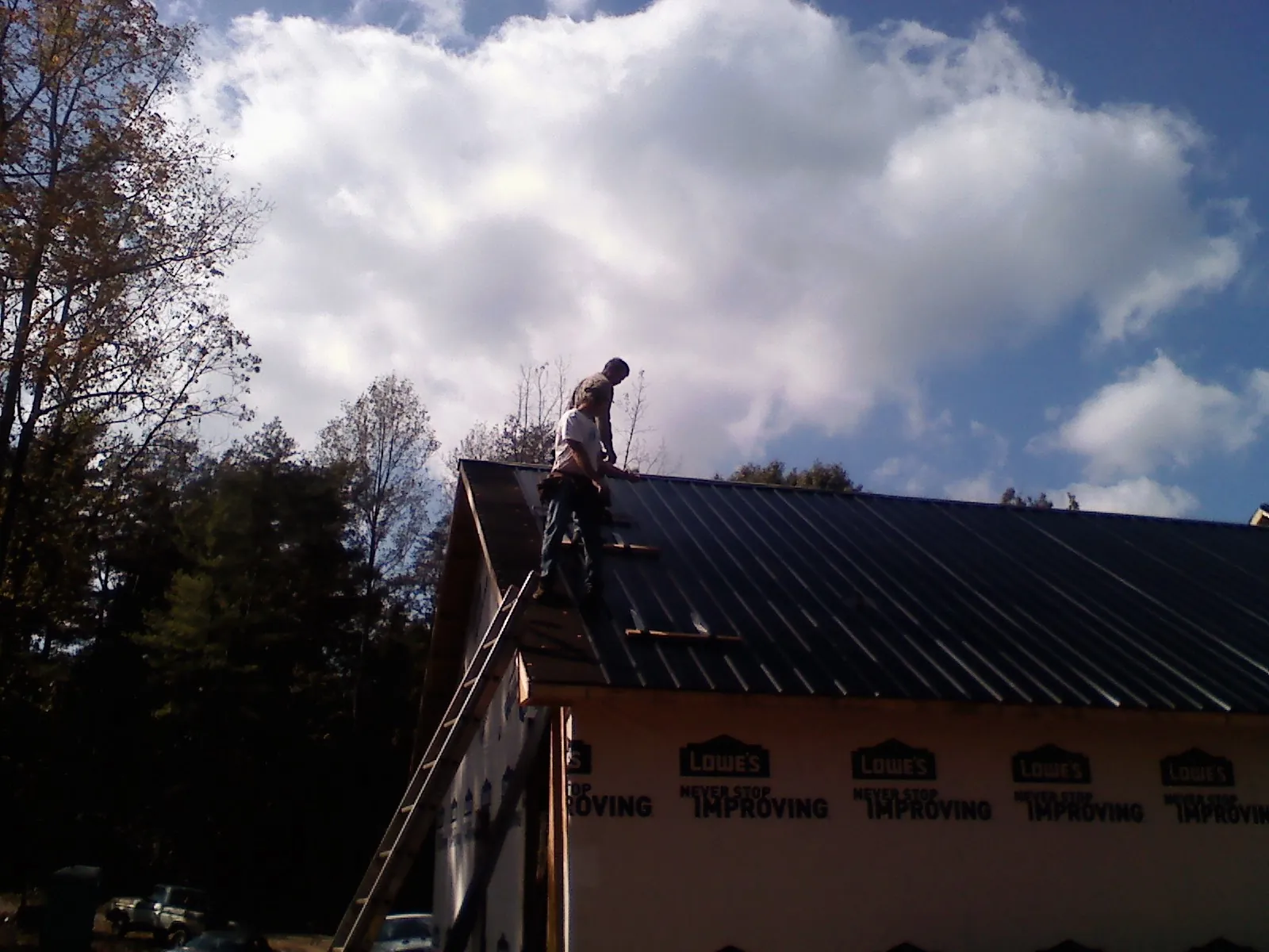 Roofer fastening dark metal panels high against a cloudy sky, from a Roof Inspection job in Winger